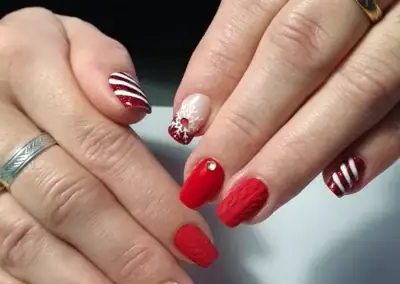 Nail art de Noël avec ongles décorés de motifs festifs et de paillettes rouges et blanches en verni permanent